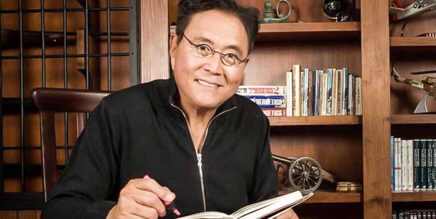 Robert Kiyosaki, autor de Pai Rico Pai Pobre, apontando para gráfico de investimentos com foco em Bitcoin, ouro e prata para crise de 2025.