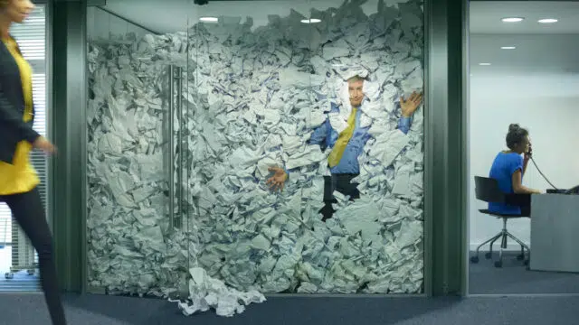 O currículo está morrendo: como a IA revolucionou o recrutamento 5 Um empresário está preso em seu escritório de vidro por um excesso de ideias descartadas no papel. Seu colega no escritório ao lado está trabalhando com mais eficiência.