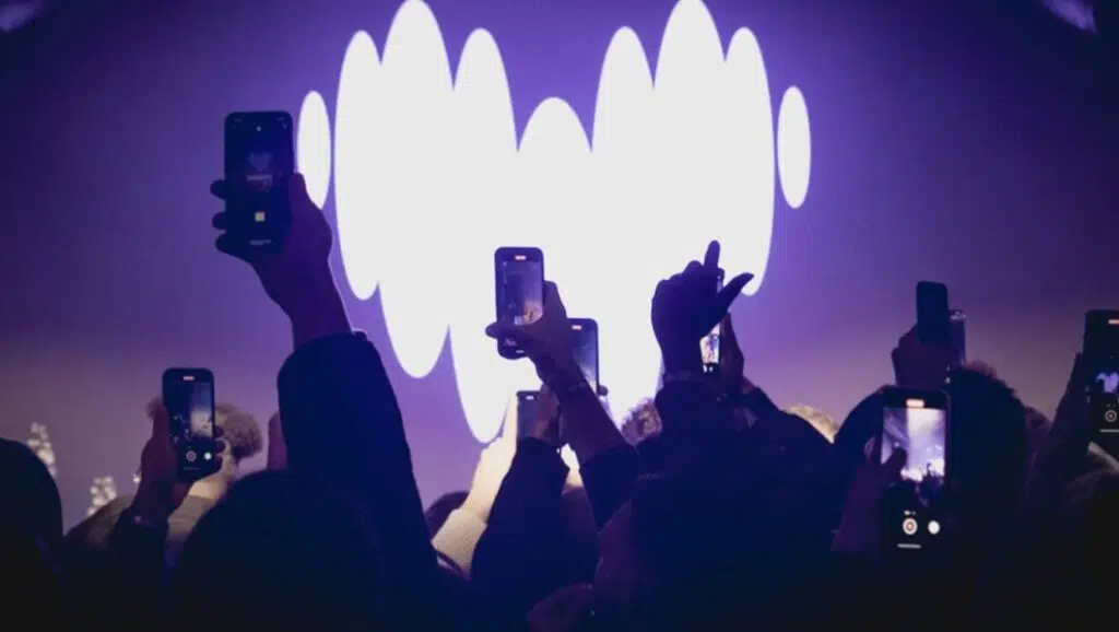 Deezer lança sistema para detectar músicas geradas por IA 5 Palco com o logotipo da Deezer ao fundo, simbolizando grandes eventos da música digital; plataforma investe em políticas para valorizar artistas legítimos e proteger o mercado.
