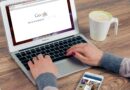 Mãos digitando no MacBook Air com a pesquisa do Google aberta e café por perto.