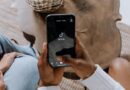 Close-up de mãos segurando um smartphone exibindo a interface do aplicativo TikTok em uma superfície de madeira.
