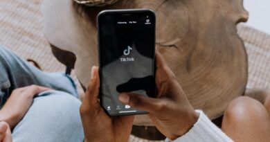 Close-up de mãos segurando um smartphone exibindo a interface do aplicativo TikTok em uma superfície de madeira.