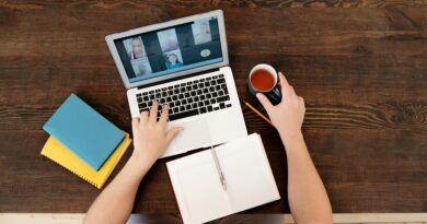 Uma pessoa participando de uma reunião virtual em um laptop com café e cadernos em uma mesa de madeira.