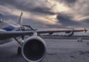 Um avião de passageiros está estacionado na pista ao pôr do sol, com outra aeronave ao fundo.