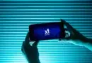 Pessoa segura telefone exibindo logo da inteligência artificial Grok, do Elon Musk, com fundo azul; polêmica sobre discurso antissemita em 2025 na X.