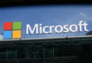 Fachada de um escritório da Microsoft; logotipo iluminado em azul sob céu nublado