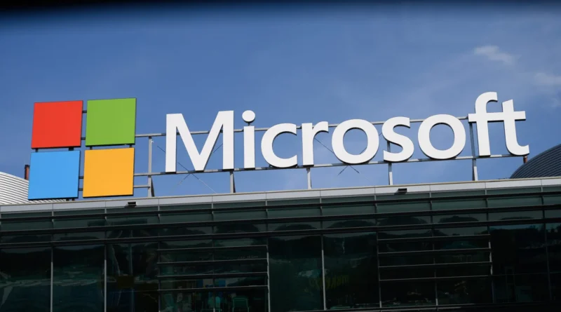 Fachada de um escritório da Microsoft; logotipo iluminado em azul sob céu nublado