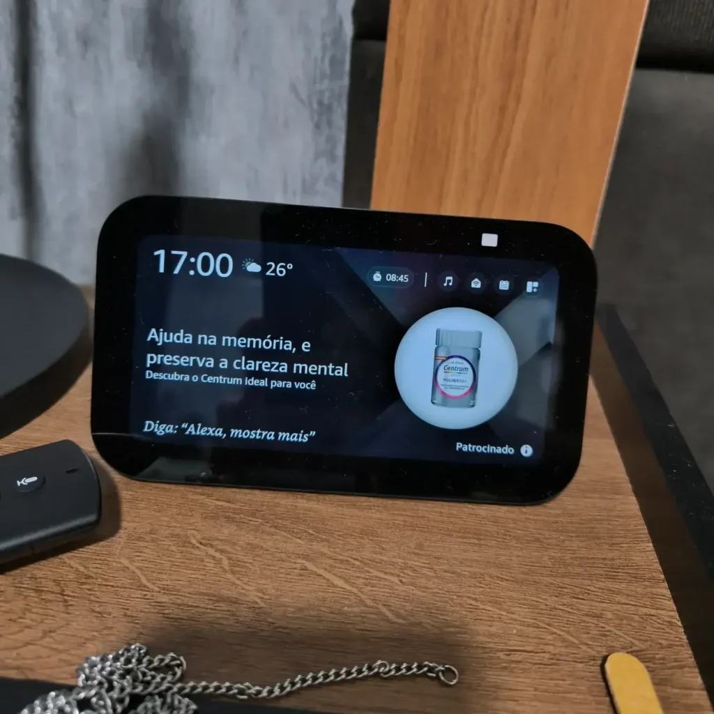Echo Show exibe publicidade irremovível: entenda 3 Detalhe do Echo Show com banner publicitário em destaque na tela ambiente, sobrepondo fotos e widgets